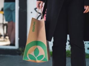 A woman carrying a brown paper bag with green logo as a plastic bag ban alternative